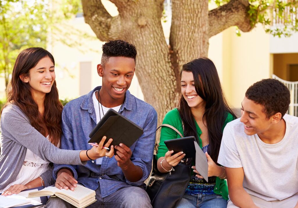 group of four students sitting side by side and looking at a tablet