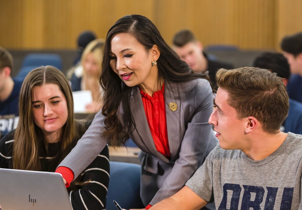 Teacher helping 2 students, one of them wearing a ORU shirt